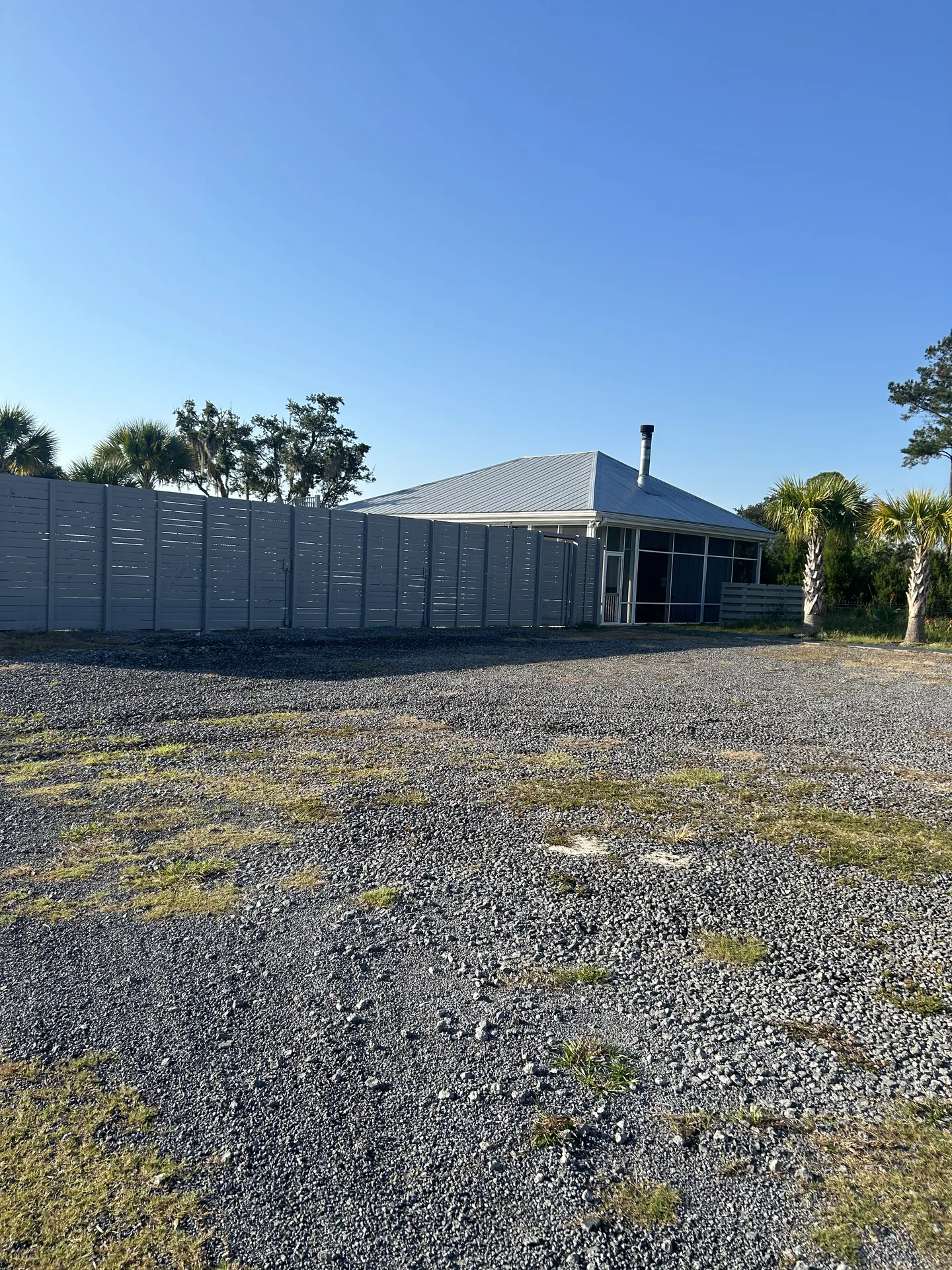 Compound perimeter with tall gray privacy fence, palmettos, and screened pavilion