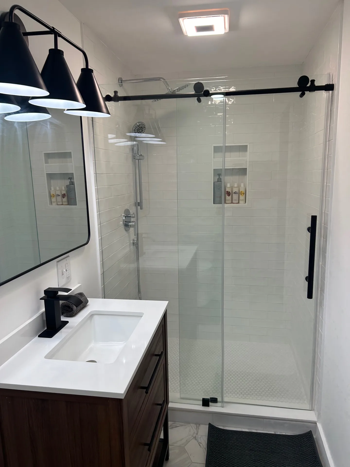 Modern bathroom with dark walnut vanity, matte black barn-door shower glass, and subway tile