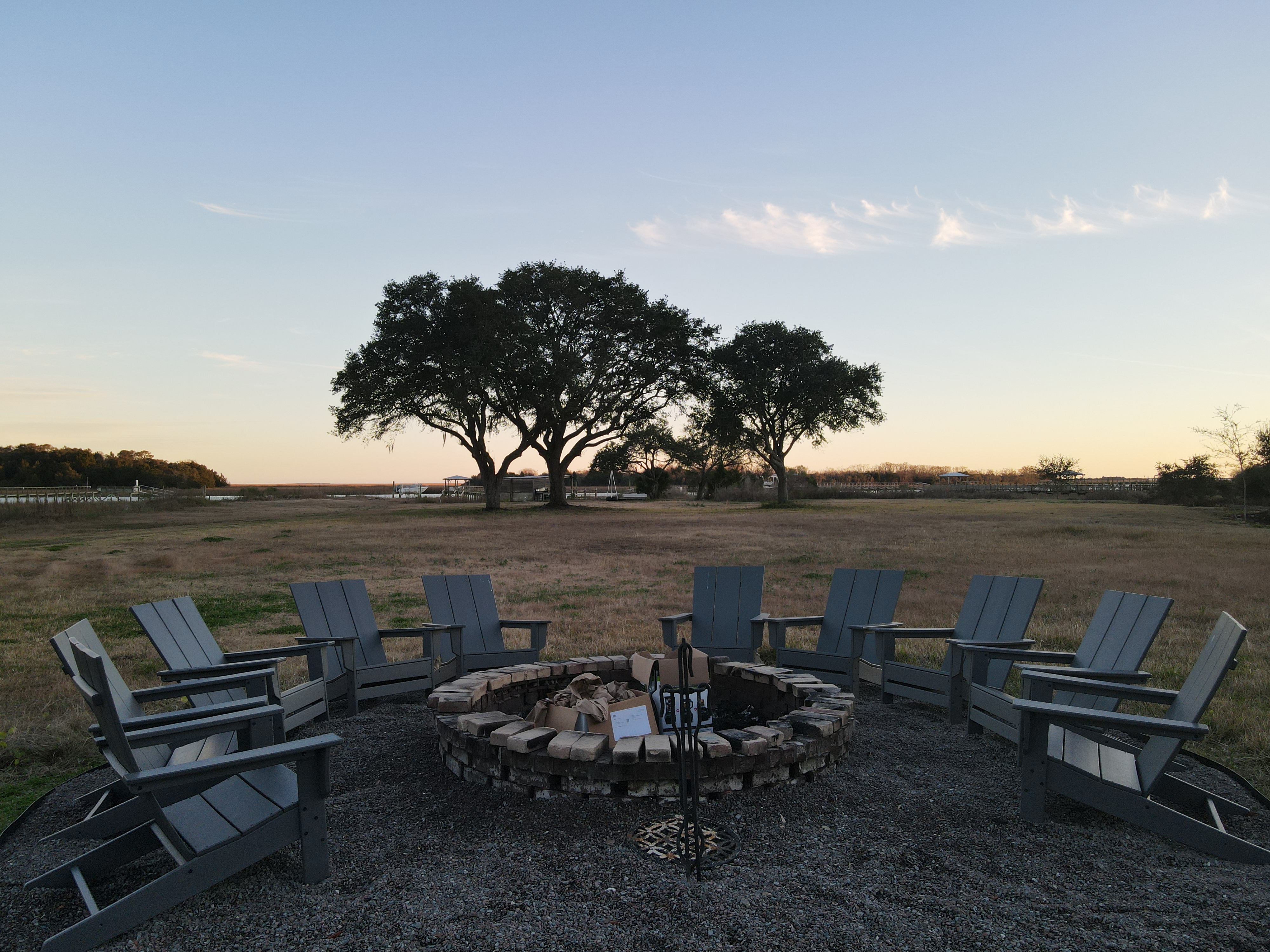 Stone fire pit under ancient live oaks with the waterway glowing at sunset