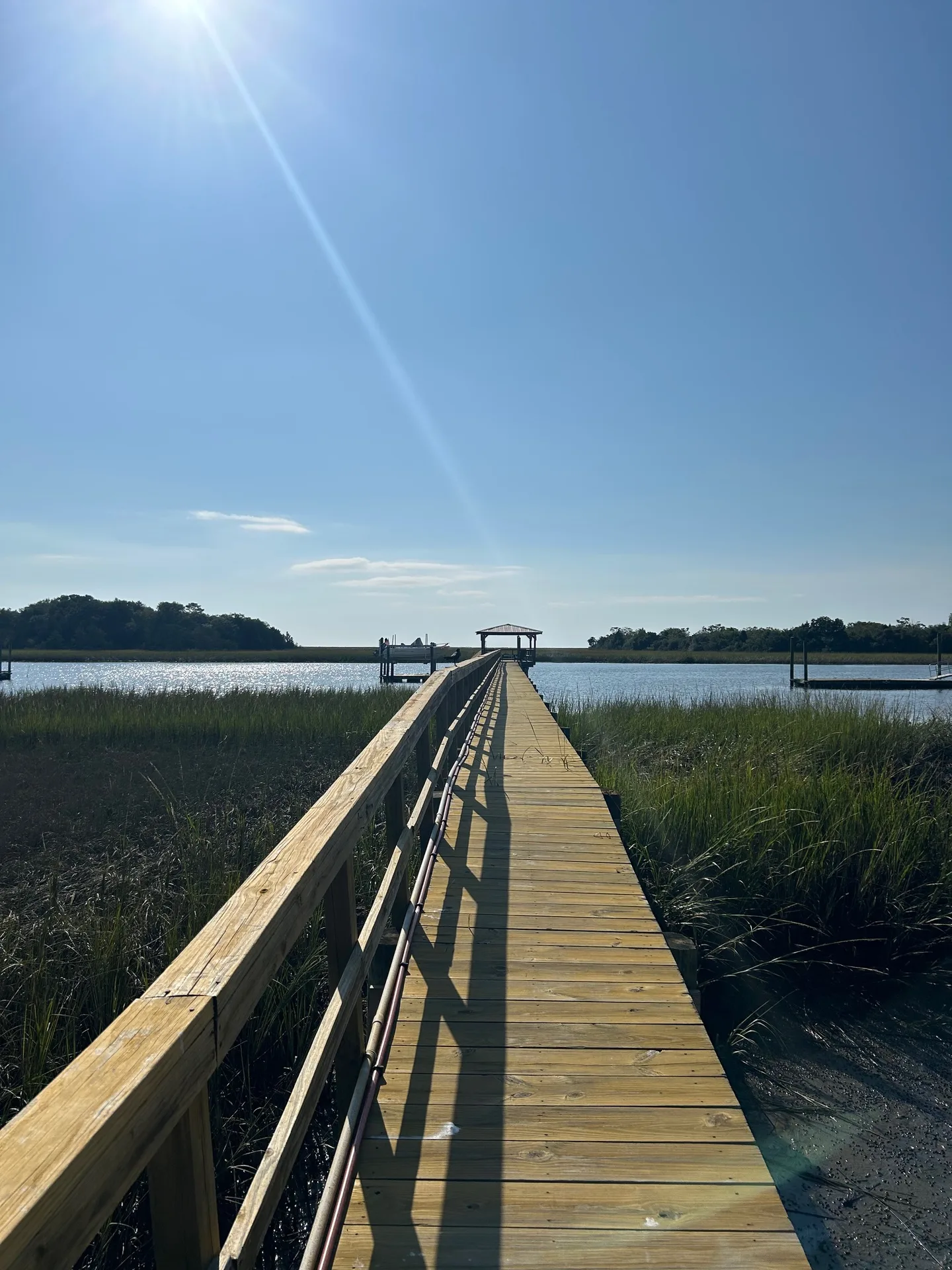 Long wooden dock stretching through green Spartina marsh to the covered boathouse