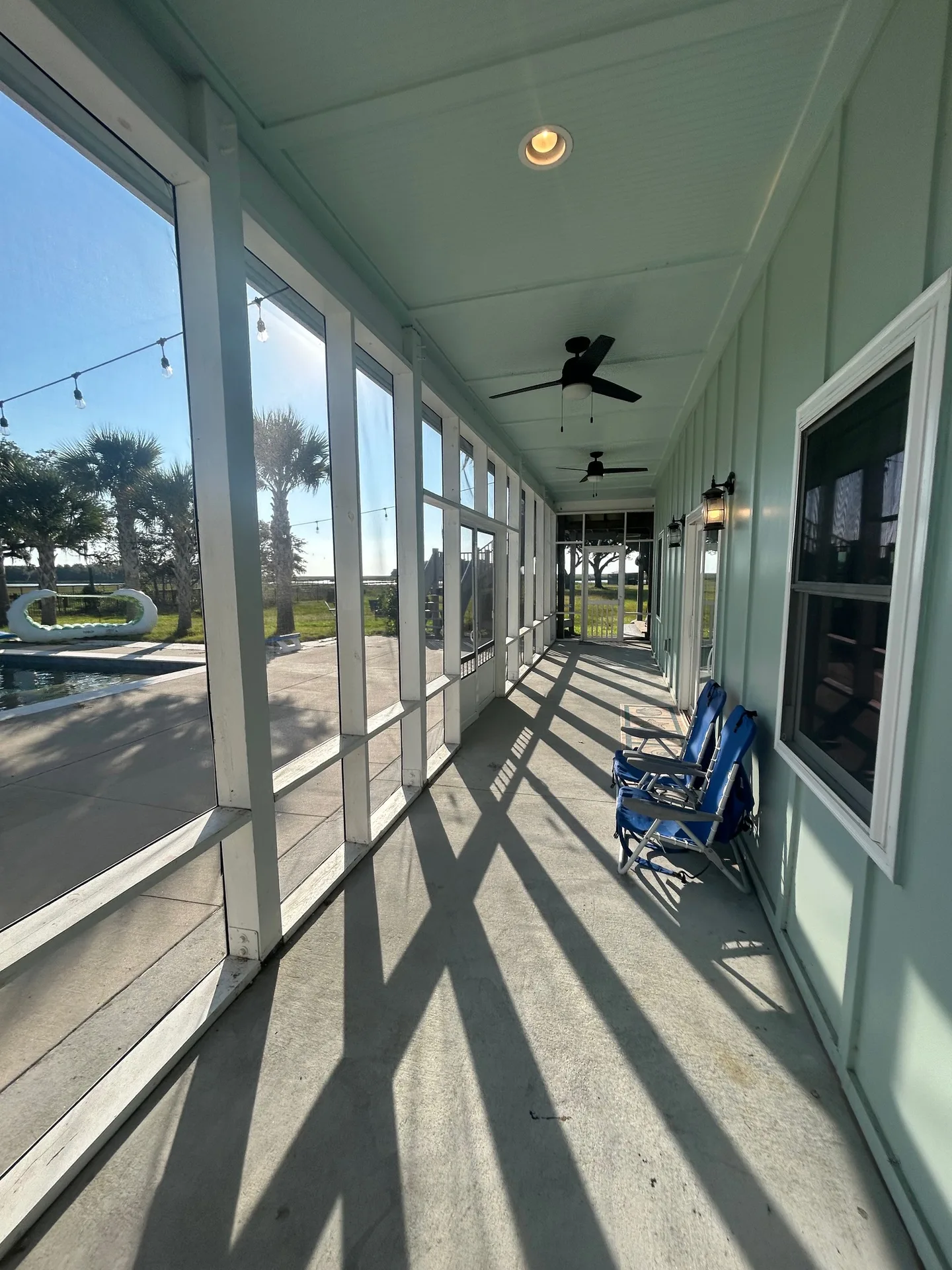 Covered veranda with twin ceiling fans and screened panels framing pool views