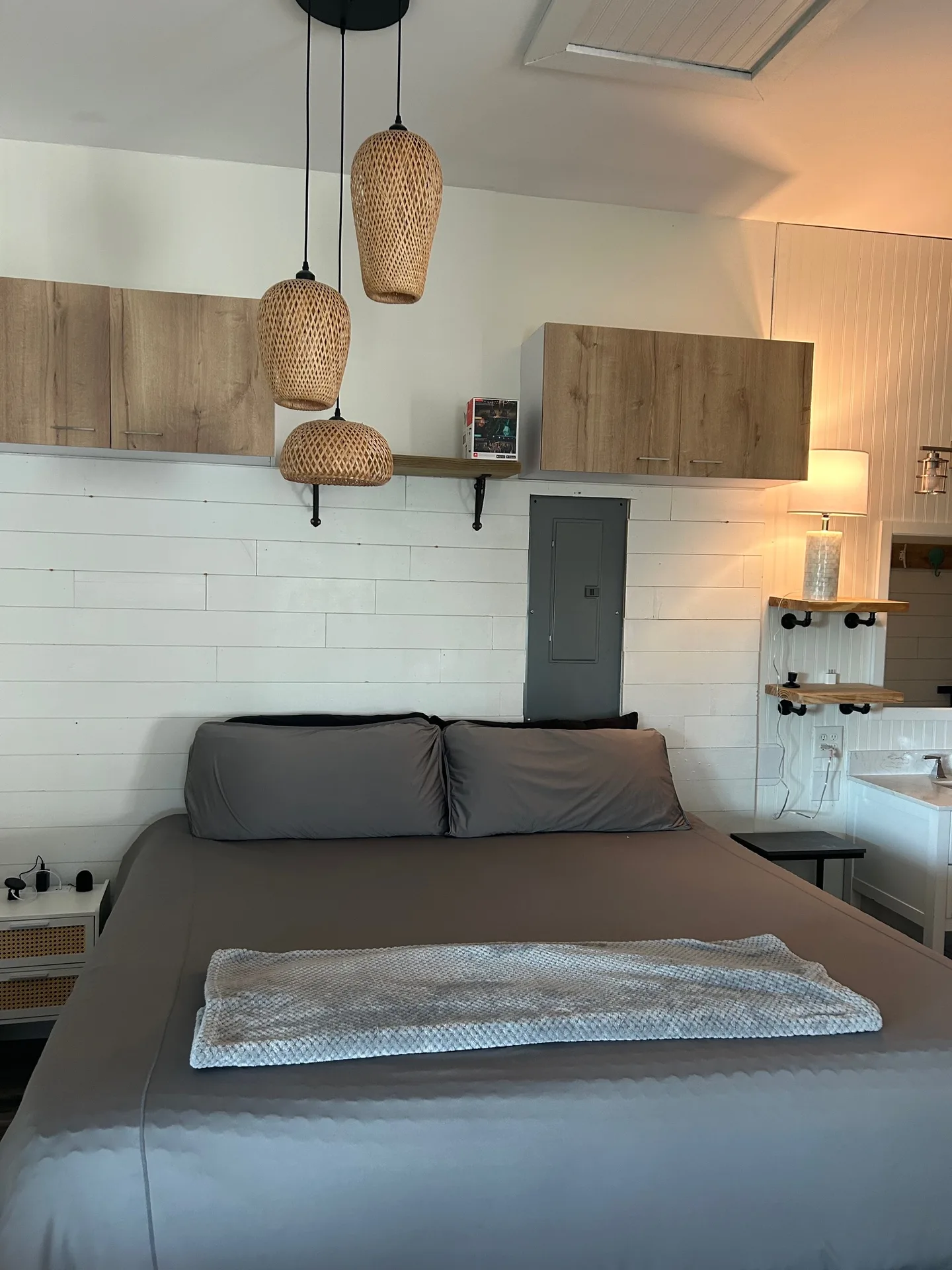 Bedroom with queen bed, trio of rattan pendant lights, and oak wall cabinets