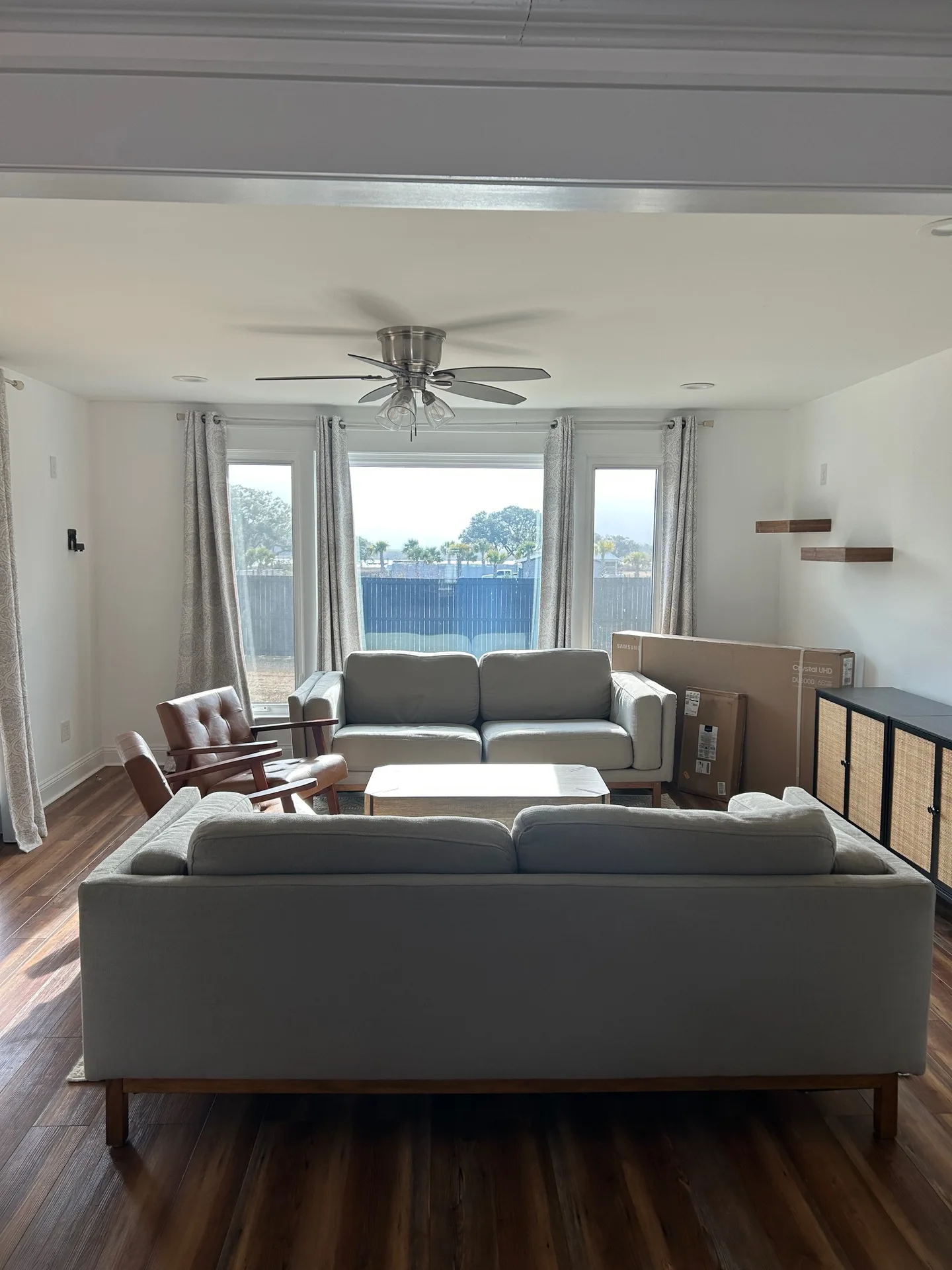Main living room with two gray sofas, cognac chair, and large windows